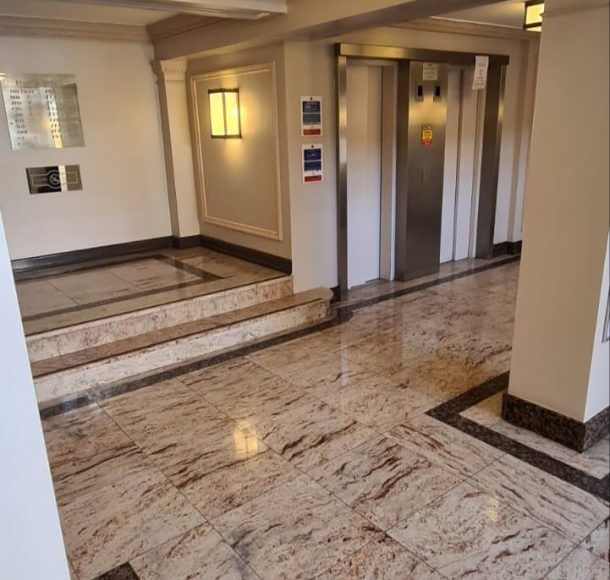 Our team of professional cleaners wearing uniforms and gloves, cleaning a communal area with modern equipment, including a vacuum cleaner, mop, and bucket. The area is clean and well-maintained, with floors and windows shining, and trash cans neatly placed in the corner.